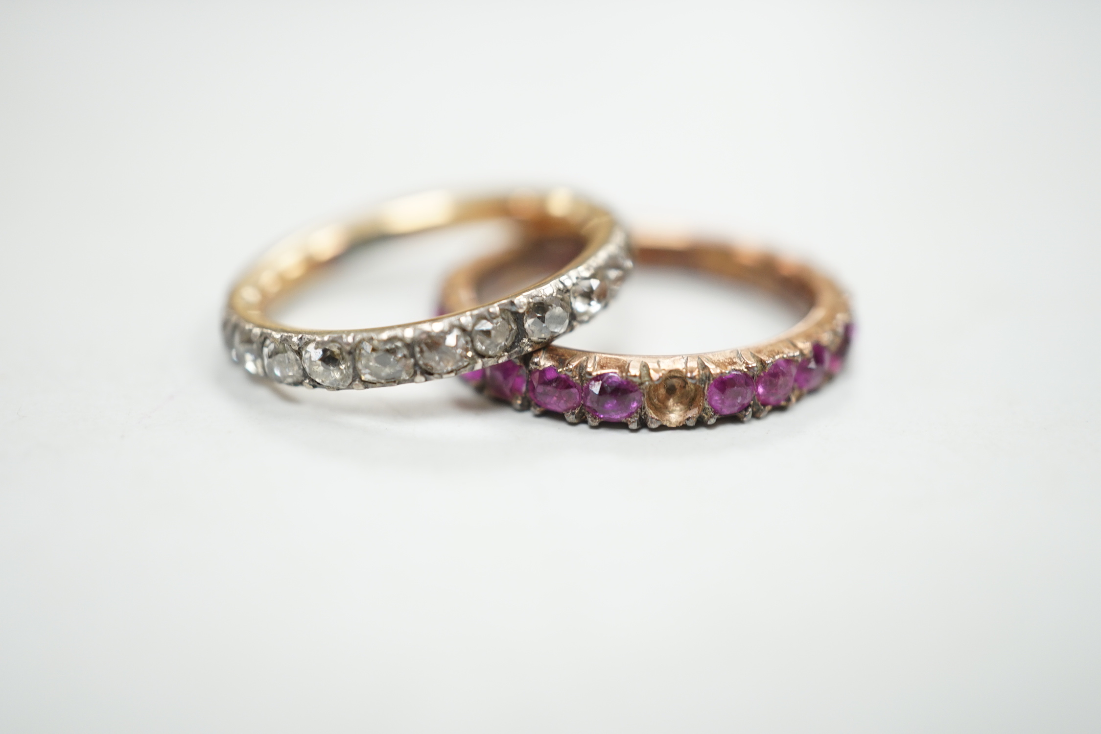 An antique yellow metal and diamond set full eternity ring (stone missing), size L and a similar pink stone set eternity ring.